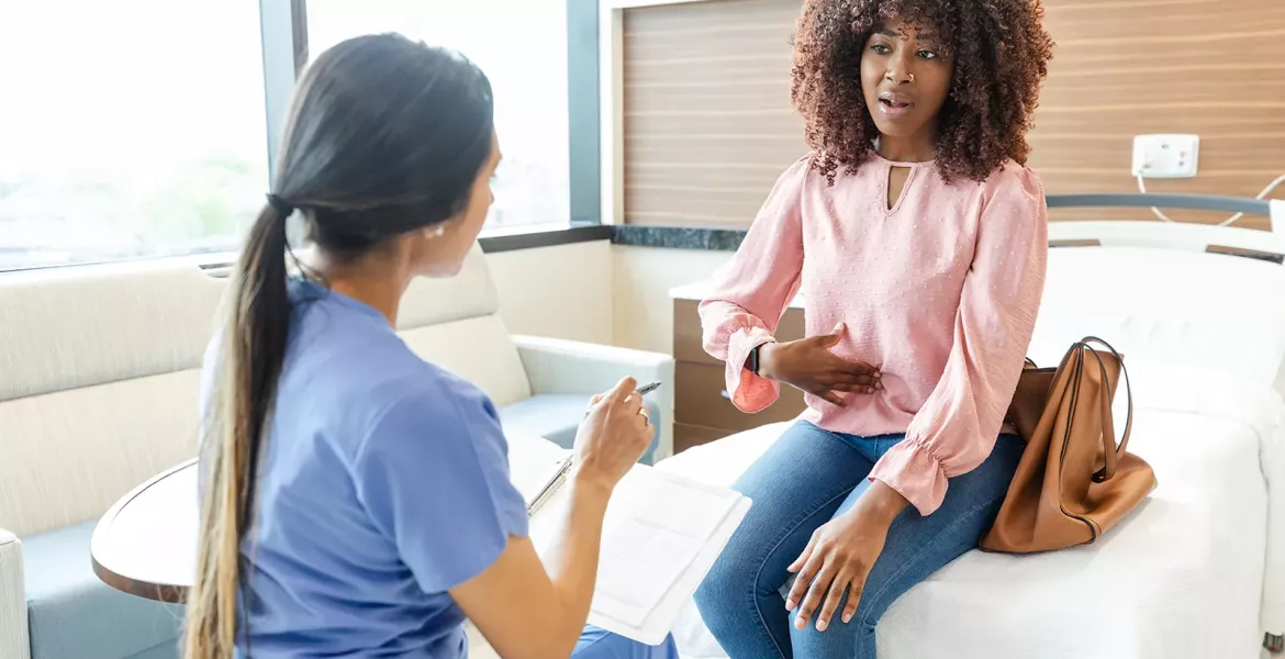 A Black female client points to her stomach in discussion with a therapist.