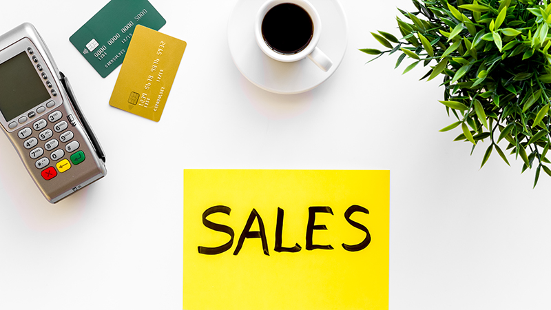 Sales sing on white background with POS payment terminal and credit cards, top view.