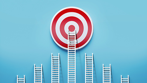 Ladders leaned up against a blue wall, with the tallest ladder reaching the center of a target