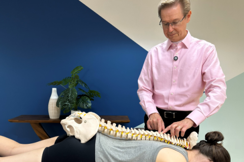 Doug Nelson points to a skeletal spine that rests on the back of a massage therapy client.