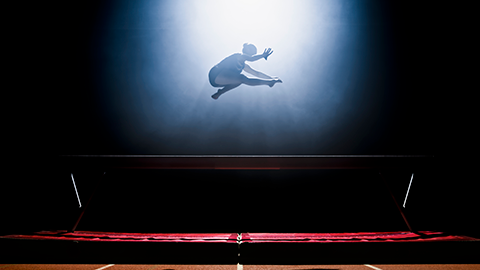 Female gymnast performing on balance beam during practice in sports hall.