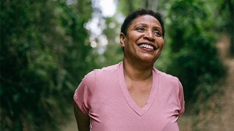 A woman smiling against a background of green trees.
